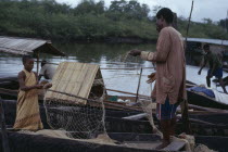 Fisherman and young girl untangling nets in wooden canoes.