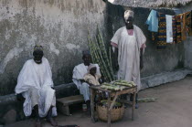 Three traditionally dressed men with little girl selling sugar cane from roadside stall.