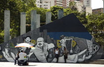 A street scene close to Teatro Teresa Careno  including two men leaning against a mural and refreshment vendor.