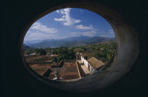 View across red tiled city rooftops framed by oval window in Iglesia San Franciso de Paula.church