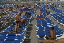 Crowded beach with rows of blue sun loungers and sunbathers. Catalunya