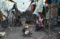 Group of laughing women and children in shanty village sitting outside underneath washing line.