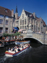 Tourists on canal boat trips below a bridge and old buildings