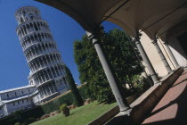 Angled view of the Leaning Tower  viewed from the grounds of the Museo del Duomo.  Framed by arch in colonnaded arcade in the foreground.