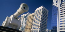 Al-Ittihad Square.  Angled view of huge sculpture of a cannon with modern high rise buildings behind. United Arab Emirates