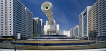 Al-Ittihad Square with huge sculpture of a cannon set on a circular tiered waterfall with modern high rise buildings on each side. United Arab Emirates