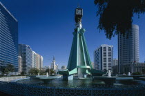 City centre clock tower with fountain underneath modern structure.  High rise buildings at each side.Center United Arab Emirates