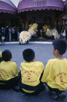 Chinese New Year Dragon Dance with three children from the troupe in the foreground watching two dragons