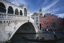 The Rialto bridge and a gondola with passengers  the Rialto Hotel in the background.