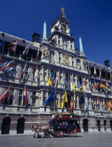 A horse drawn tourist coach in front of the Town Hall which is covered in flags.