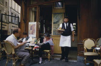 A waiter carrying a tray with drinks to customers sat outside la Palette Cafe.