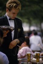 Formal waiter standing at a table with drinks on and holding a silver tray