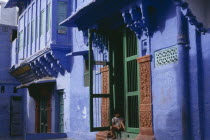 Detail of blue painted house with child sitting in open doorway with green frame and decorated surround.