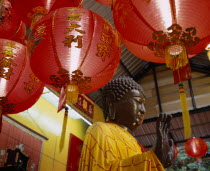 Charoen Krung.  Buddha statue bathed and dressed in auspicious gold and red silk for Chinese New Year with red New Year lanterns in the foreground. New Road