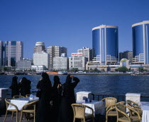 Dubai Creek.  Women in waterfront restaurant on Bur Dubai city side looking out towards city skyline on Deira side.Dubayy United Arab Emirates