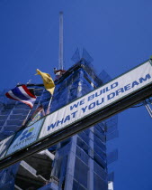 Looking up at sign  We Build What You Dream  with high rise building under construction behind.