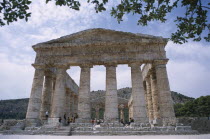 Doric Temple. Ruins of the ancient city. Colonnaded structure framed by tree branches with visitors walking aroundTemple of Segesta