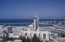 Elevated view of downtown area with modern tall buildings including a fish shaped skyscraper towards the docks and coastline in the background