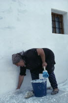 Andalucian village woman white washing the exterior wall of her home.Andalusia