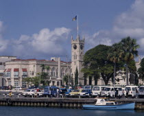 The Carenage. Buildings and church clock tower with cars on quay and a boat on water