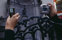 Cropped view of visitors to the Manneken-Pis statue holding up digital camera and mobile phone to take photograph.