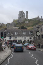 View from road with traffic towards cottages overlooked by Corfe Castle behind Great Britain United Kingdom UK