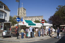 French Market. People gathered around covered market stalls with the Church of St Mary de Haura behind.Great Britain United Kingdom UK