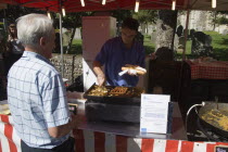 French Market. Food stall with stallholder cooking sausage and onion baguettes with a male customer waitingGreat Britain United Kingdom UK