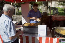 French Market. Food stall with stallholder cooking sausage and onion baguettes with a male customer waitingGreat Britain United Kingdom UK