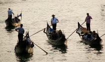 Gondoliers carrying sightseeing tourists on their gondolas at sunset on the Grand Canal