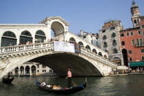 Gondolas carrying sightseeing tourists pass under the Rialto Bridge lined with people