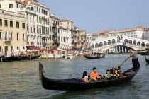 Sightseeing tourists in a Gondola on the Grand Canal with the Rialto Bridge behind them