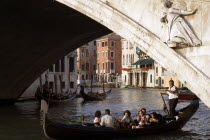 A gondola carrying tourists passes beneath the Rialto Bridge over the Grand Canal