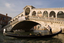 An empty gondola passes in front of the Rialto Bridge over the Grand Canal at sunset