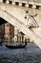 A gondola carrying tourists passes beneath the Rialto Bridge over the Grand Canal