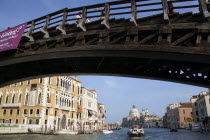 The Byzantine church of Santa Maria della Salute with water taxis and a motoscafo passing along the Grand Canal towards Palazzo Franchetti Cavali decked with flags. People walk across the wooden Accad...