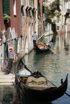 A Gondola with tourists passing along a canal in the San Marco district. Another gondolier waits by some steps for passengers