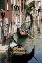 A Gondola with tourists passing along a canal in the San Marco district. Another gondolier waits by some steps for passengers