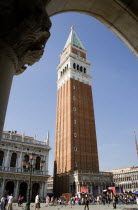 The Campanile in Piazza San Marco seen through an arch below the Doges Palace with tourists walking in the square