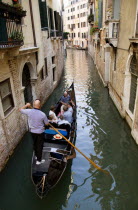 Gondolier carries sightseeing tourists in his gondola along a norrow canal in the San Marco disrtrict