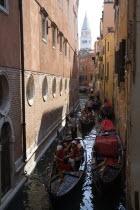 Gondoliers carry sightseeing tourists in gondolas along the norrow Rio di San Salvador canal with the Campanile in the distance in Piazza San Marco