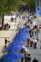 The Paris Plage urban beach. People strolling between the River Seine and people playing boules or petanque divided by a line of tables under umbrellas along the Voie Georges Pompidou usually a busy r...