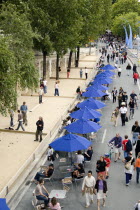 The Paris Plage urban beach. People strolling between the River Seine and people playing boules or petanque divided by a line of tables under umbrellas along the Voie Georges Pompidou usually a busy r...