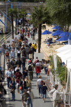 The Paris Plage urban beach. People strolling between the River Seine and people lying on sand along the Voie Georges Pompidou usually a busy road now closed to traffic opposite the Ile de la Cite