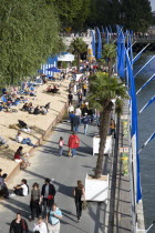 The Paris Plage urban beach. People strolling between the River Seine and other people lying on sand along the Voie Georges Pompidou usually a busy road now closed to traffic