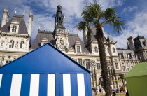 The Paris Plage urban beach. Young people playing beach volleyball behind beach huts in front of the Hotel de Ville Town Hall