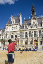 The Paris Plage urban beach. Young people playing beach volleyball in front of the Hotel de Ville Town Hall with a young man serving