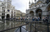 Aqua Alta High Water flooding in St Marks Square with tourists on elevated walkways above the flooded piazza beside St Marks Basilica and the Torre dellOrologio clock tower