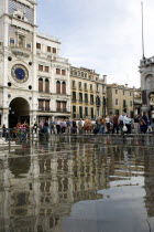 Aqua Alta High Water flooding in St Marks Square with tourists on elevated walkways above the flooded piazza beside St Marks Basilica and the Torre dellOrologio clock tower