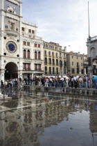 Aqua Alta High Water flooding in St Marks Square with tourists on elevated walkways above the flooded piazza beside St Marks Basilica and the Torre dellOrologio clock tower